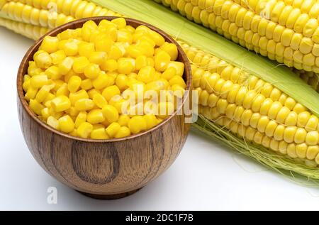 Sweet corn grains in wooden bowl on the background of fresh corn cobs. Fresh sweet corn top view. Stock Photo
