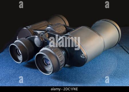 The Binoculars rests upon turn blue the table on black background. Equipment for observation in distance Stock Photo