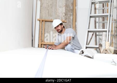 construction worker plasterer man measuring wall with measure tape in building site of home renovation with tools and building materials on the floor Stock Photo