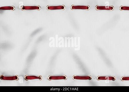 Red satin ribbon inserted in the gold rings on white silk, trendy background Stock Photo