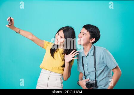 Portrait happy Asian young handsome man, beautiful woman couple smile standing wear shirt, taking selfie photo on a smartphone, studio shot on blue ba Stock Photo