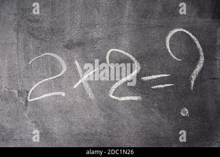mathematical example two times two is written in white chalk on a black chalk board, close up Stock Photo