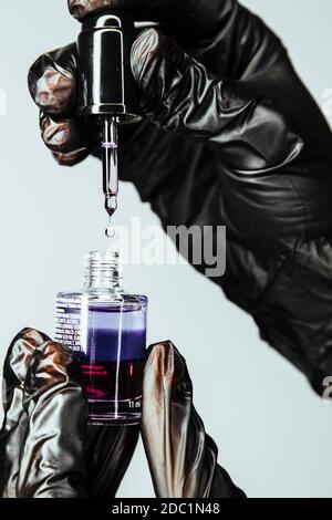 Cosmetic oil for salon procedures. A drop of product is visible on the oil dispenser. Hands in black gloves hold nail and cuticle care product. Stock Photo