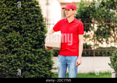 A uniformed courier holds a paper box in the open air. Delivery service Stock Photo