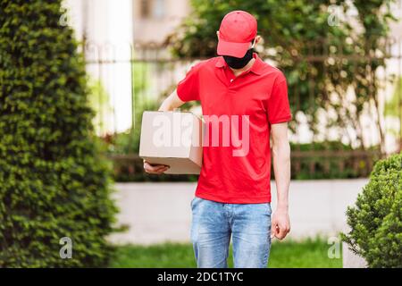 A courier in a protective medical mask with boxes in his hands delivers parcels. Service delivery in terms of quarantine, pandemic coronavirus Stock Photo