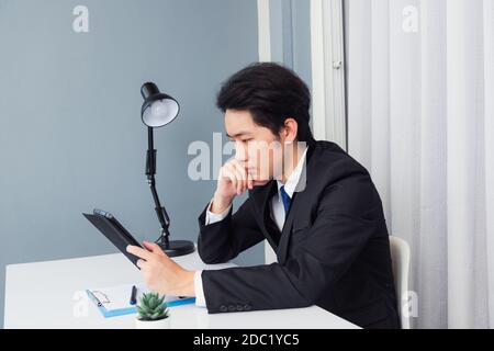 Work from home, Asian young businessman video conference call or facetime he smiling looking to tablet sitting on desk using smart tablet computer and Stock Photo
