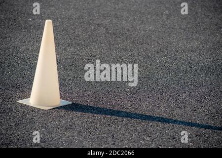 Full frame image with copy space shot in natural light. White plastic cone glows in golden hour sun and casts a long shadow on the black asphalt. Stock Photo