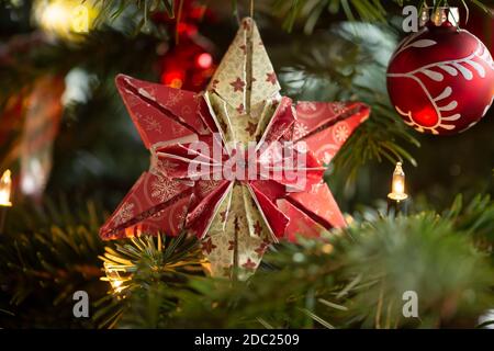 Decorated Christmas tree, real Nordmann fir in front of blurred background. Macro photography shows a 6 pointed star folded from paper. Stock Photo