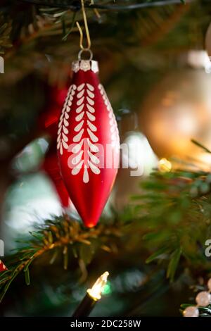 Decorated Christmas tree, real Nordmann fir in front of blurred background. Macro photography shows a red glass cone with white ornaments. Stock Photo