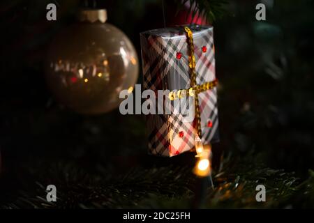 Decorated Christmas tree, real Nordmann fir in front of blurred background. Macro photography shows wrapped hand made gift. Dark mood. Stock Photo