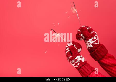 cropped view of woman in mittens holding sparklers isolated on red Stock Photo