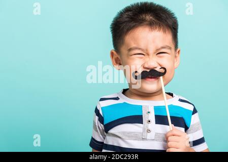 Funny happy hipster kid holding black mustache props for the photo booth close face, studio shot isolated on a blue background, Men health awareness, Stock Photo