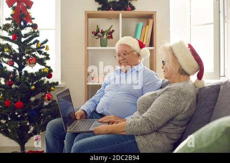 Side view of happy senior couple using laptop watching favorite Christmas movies. Stock Photo