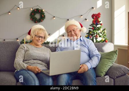 Smiling senior couple sitting on sofa at home and video calling family using laptop Stock Photo