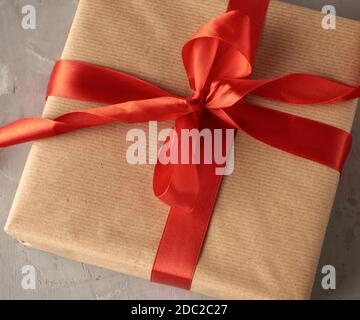 knotted bow made of red silk ribbon on brown kraft paper background, festive backdrop Stock Photo