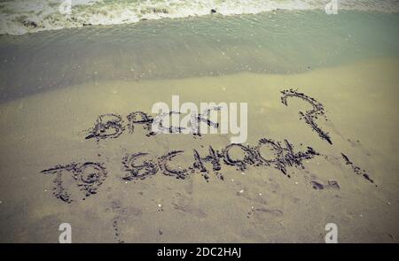 Big text BACK TO SCHOOL written in the sand of the beach by the sea with question mark Stock Photo