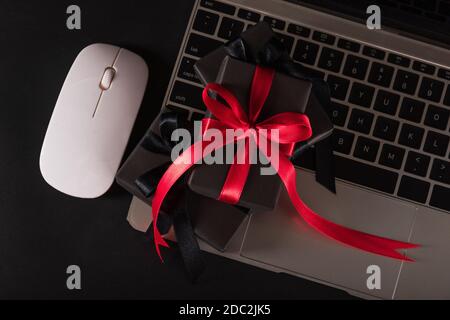 Black Friday sale online shopping commerce, Top view of gift box wrapped black paper and red bow ribbon present on a laptop computer keyboard, studio Stock Photo