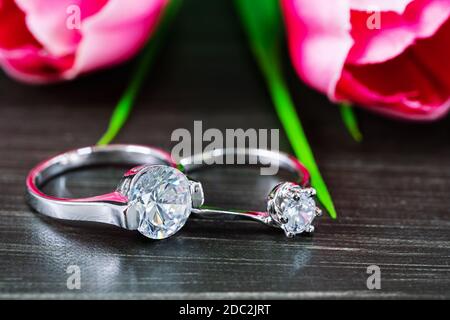 Close up Diamond gem wedding rings with pink tulip flower on black background Stock Photo