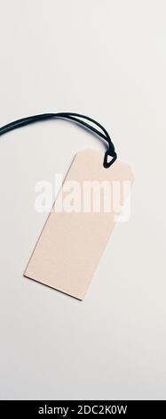 The price tag made of cardboard is empty without inscriptions on a light background. Light falls from one side, there is a shadow. Stock Photo