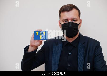 Man wear black formal and protect face mask, hold Cheshire flag card isolated on white background. United Kingdom counties of England coronavirus Covi Stock Photo