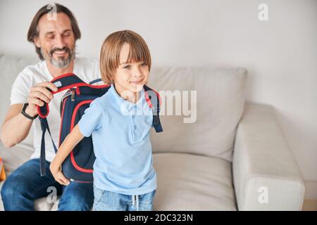 Caring father assisting his child with putting backpack on Stock Photo