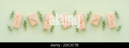 Row gift boxes wrapped in kraft paper, tied with jute twine and natural twigs of eucalyptus on green background. Holiday concept Top view Flat lay Tem Stock Photo