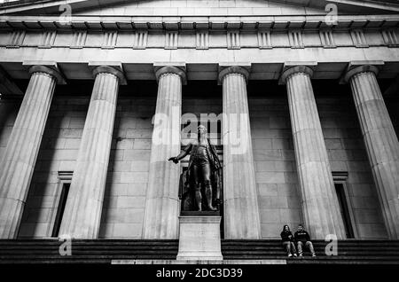 Black & White View of a Couple Sitting in Front of Federal Building in Wall Street. Greek Style Building in Financial District, Manhattan, New York Stock Photo