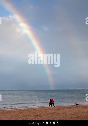 Portobello, Edinburgh, Scotland, UK. 18 November 2020. Rainbow at the seaside,10 degrees but windchill makes it feel cooler for this couple walking on the shoreline of the Firth of Forth. Credit: Arch White/Alamy Live News. Stock Photo