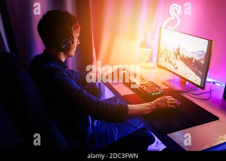 A professional gamer plays online video games in the first person on his personal computer, sitting in a room with neon lights. Online cyber sport cha Stock Photo