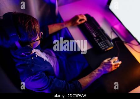 A professional gamer plays online video games in the first person on his personal computer, sitting in a room with neon lights. Online cyber sport cha Stock Photo