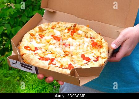 Young man is holding box with tasty pizza, close up view. Italian Cuisine. Snack on a sunny summer day. Stock Photo