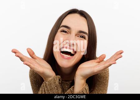 Excited young woman , casual in a golden sweater, screams happily, raises her hands up in surprise, over white studio wall with copy space Stock Photo