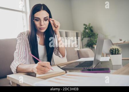 Photo of focused business woman hold pen sit sofa write notes fingers specs wear eyeglasses shirt in home workstation indoors Stock Photo