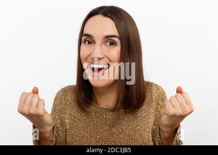 Excited young woman , casual in a golden sweater, screams happily, raises her hands up in surprise, over white studio wall with copy space.  Stock Photo