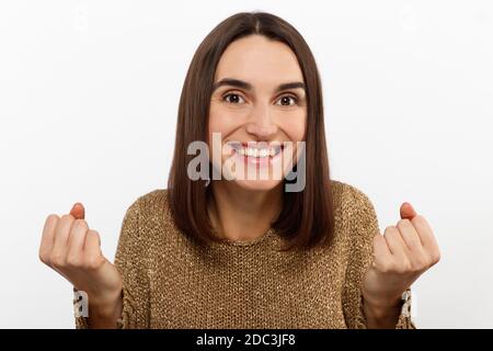 Excited young woman , casual in a golden sweater, screams happily, raises her hands up in surprise, over white studio wall with copy space.  Stock Photo