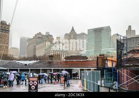 Tourists Waiting in Queue Line in Battery Park, Manhattan. Skyscraper Buildings in Background on a Rainy Day. New York City, USA Stock Photo