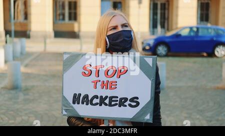 Concerned woman in protective mask with protest banner calling to stop hackers by walking on the city street Stock Photo