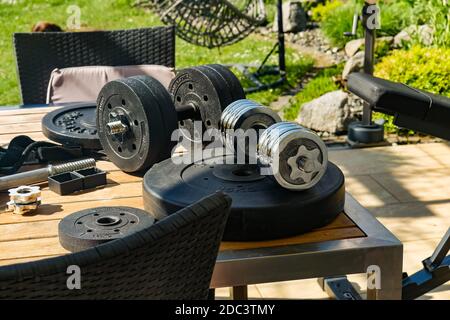 Exercise weights and adjustable dumbbells on outdoor table. High angle view. Stock Photo