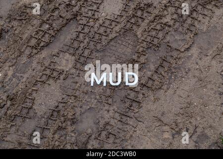 the word mud laid with silver metal letters on wet dirt surface with directly above perspective under cloudy autumn day light Stock Photo