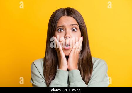 Photo of shocked impressed child girl dressed casual green outfit arms cheeks big eyes isolated yellow color background Stock Photo