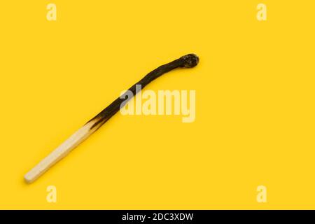 A burned macth on a yellow background with copy space Stock Photo