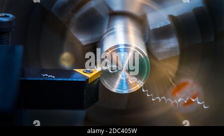 Close-up of turning. Sharp tool bit on dark background. Cutting tool with yellow triangular carbide insert on working lathe. Spiral swarf. Motion blur. Stock Photo