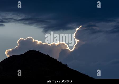 Storm clouds lit by the sunset sun behind the silhouette of a mountain Stock Photo