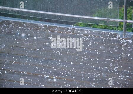 Tiny white grains of hail and rainwater cover the brown tiled balcony. Detailed close up shot of raindrops and icy soft hail falling on the wet ground during a spring thunderstorm.  Stock Photo