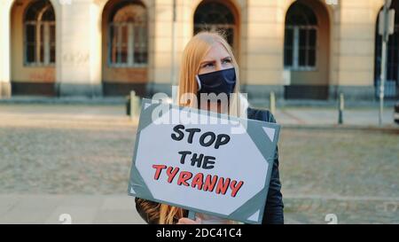 Young woman in protective mask calling to stop the tyranny by holding steamer. Protest walk in the city center. Stock Photo