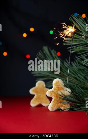 Little people made of toasted bread, sparkler, branch of New Year tree close-up on red-black background with multi-colored bokeh from garland.Christma Stock Photo