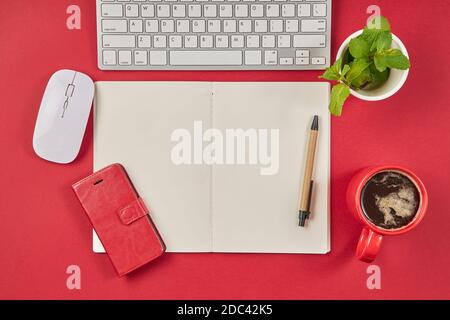 Red office desk table with blank notebook, keyboard and coffee cup. Top view with copy space. Stock Photo