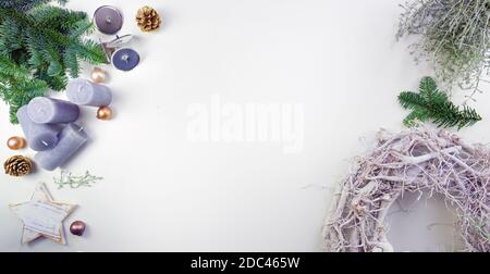 Advent and Christmas decoration with a pale wooden wreath, fir branches, lilac candles and matt golden baubles on a white table, panoramic format with Stock Photo