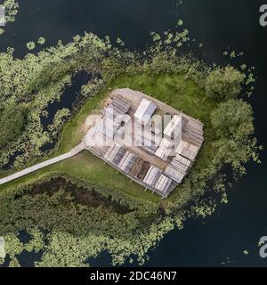 Ancient wooden settlement on river island. Green coastal thickets in dark water. Top view from above. Stock Photo