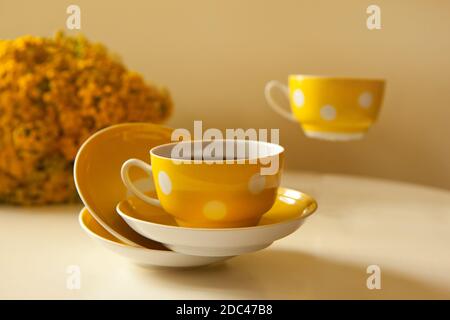 Two flying yellow coffee cups on white background, coffee break and caffeine addiction concept. yellow flowers on the table Stock Photo